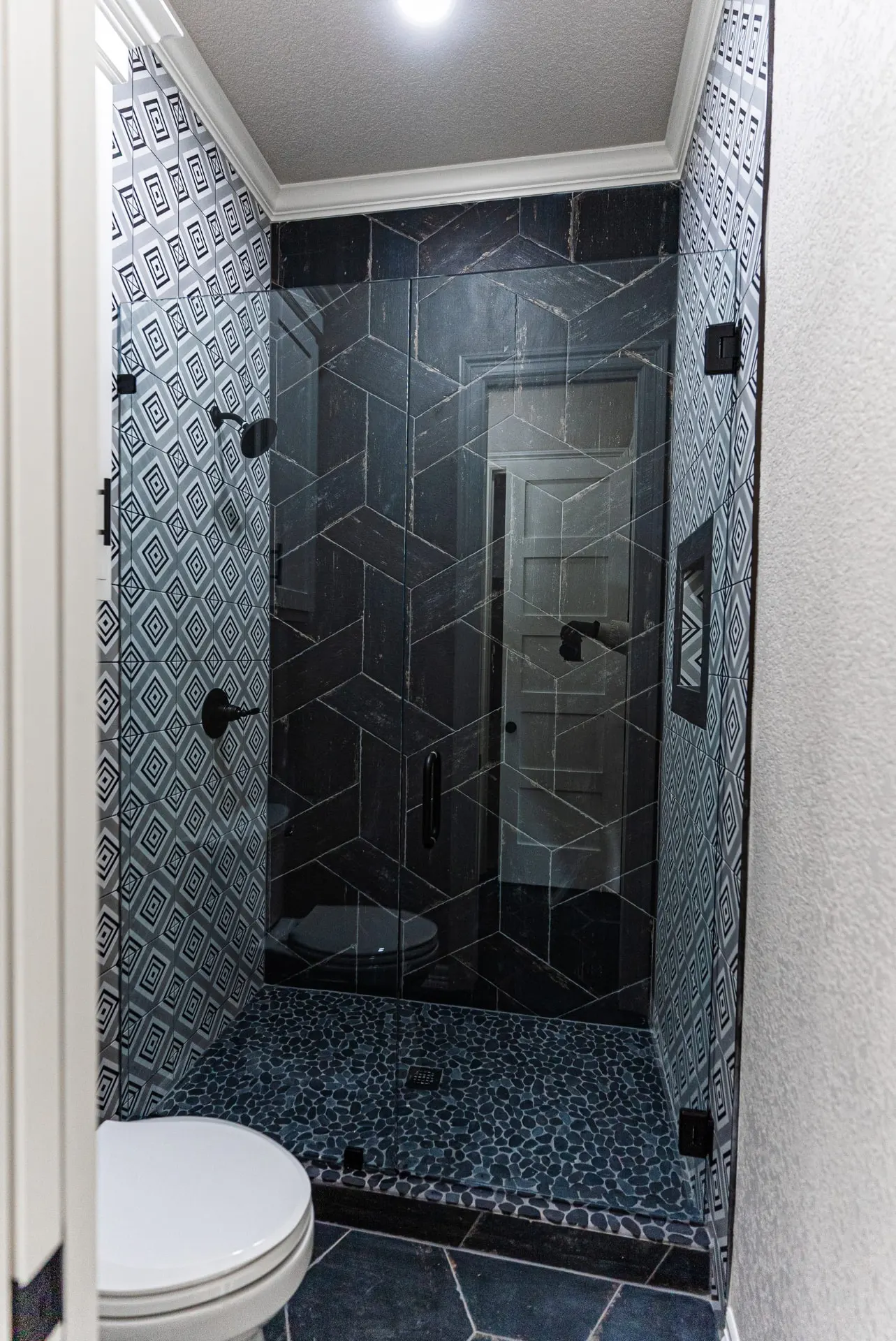 Walk-in shower at 1602 NW 12th St with black chevron marble tile, geometric gray tile walls and pebble floor