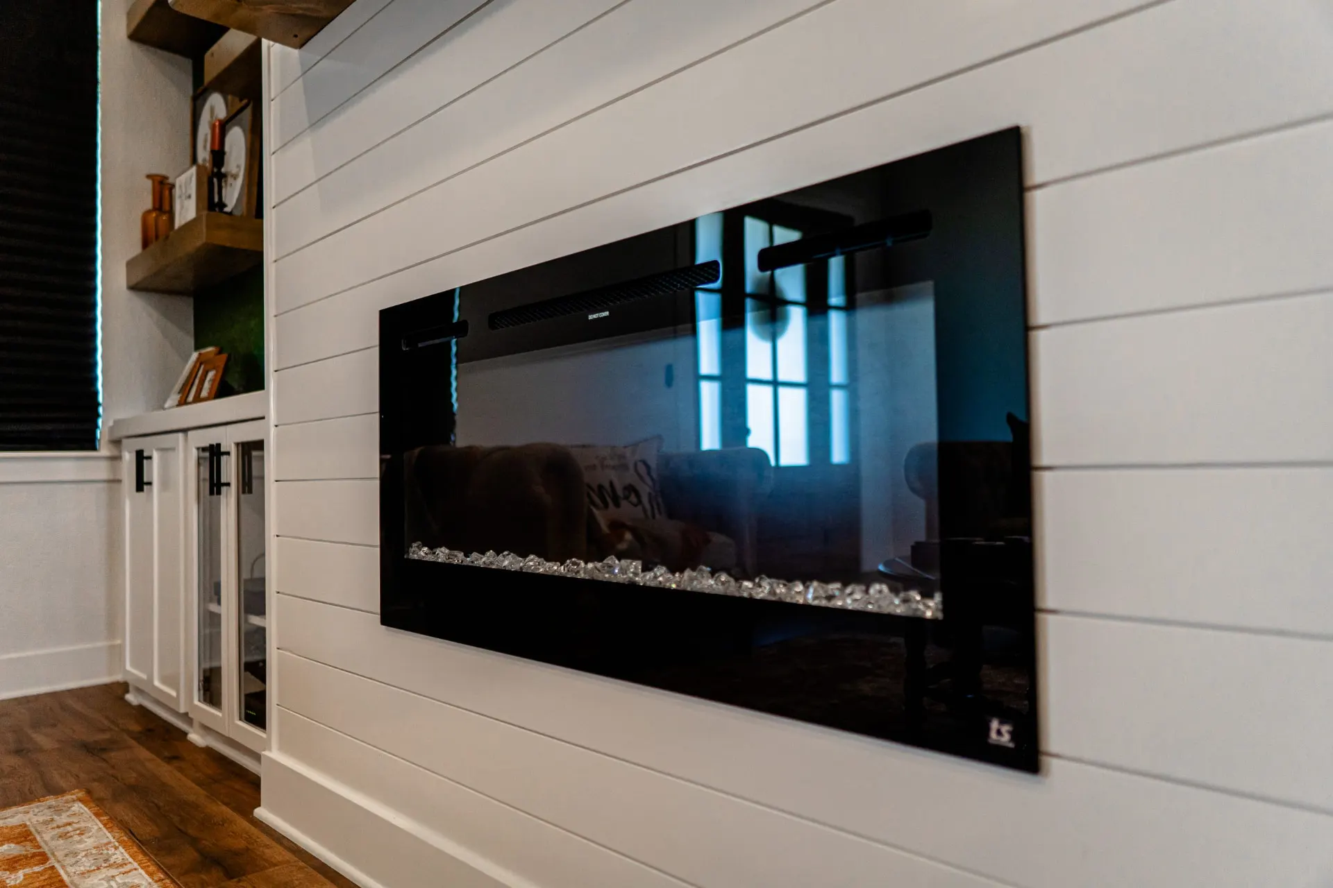 Living room at the K Ave Farmhouse with a linear electric fireplace set in a white shiplap wall, glass-front built-ins and floating wood shelves over a dark green accent wall
