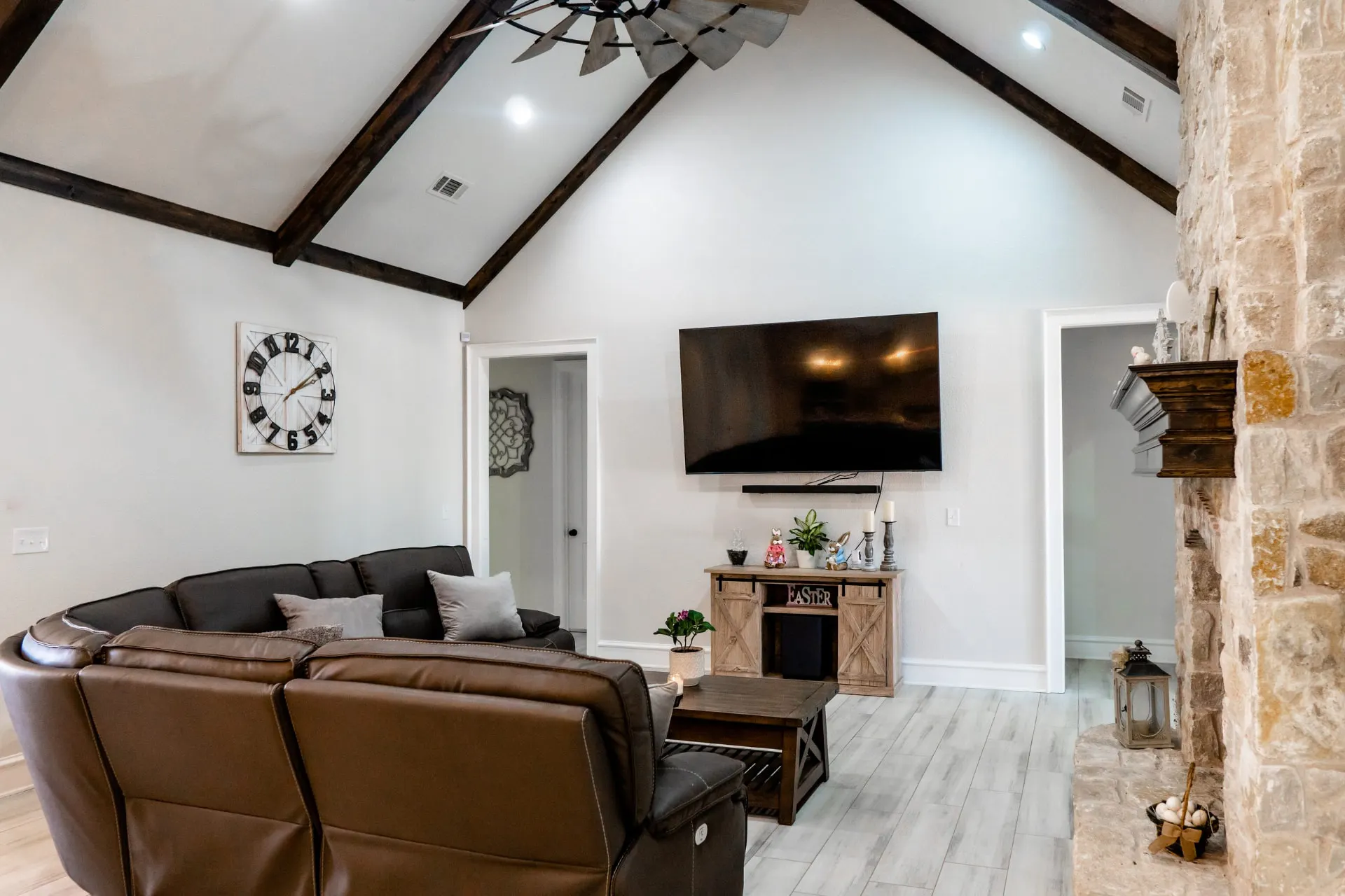 Second great-room view at 1667 Eldenrod with a square wall clock, exposed beams and a floor-to-ceiling stone fireplace