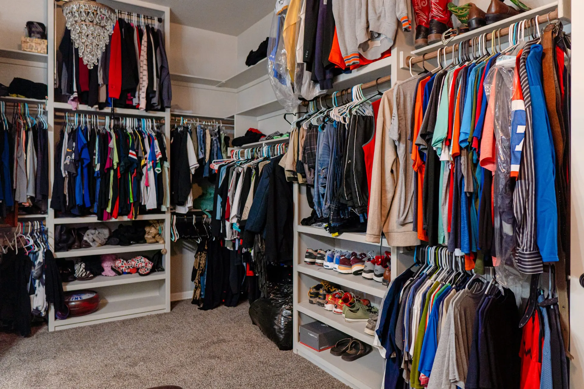 Walk-in primary closet wrapped in white built-in rods and shoe shelving under a crystal chandelier at 8821 Shawn Dr