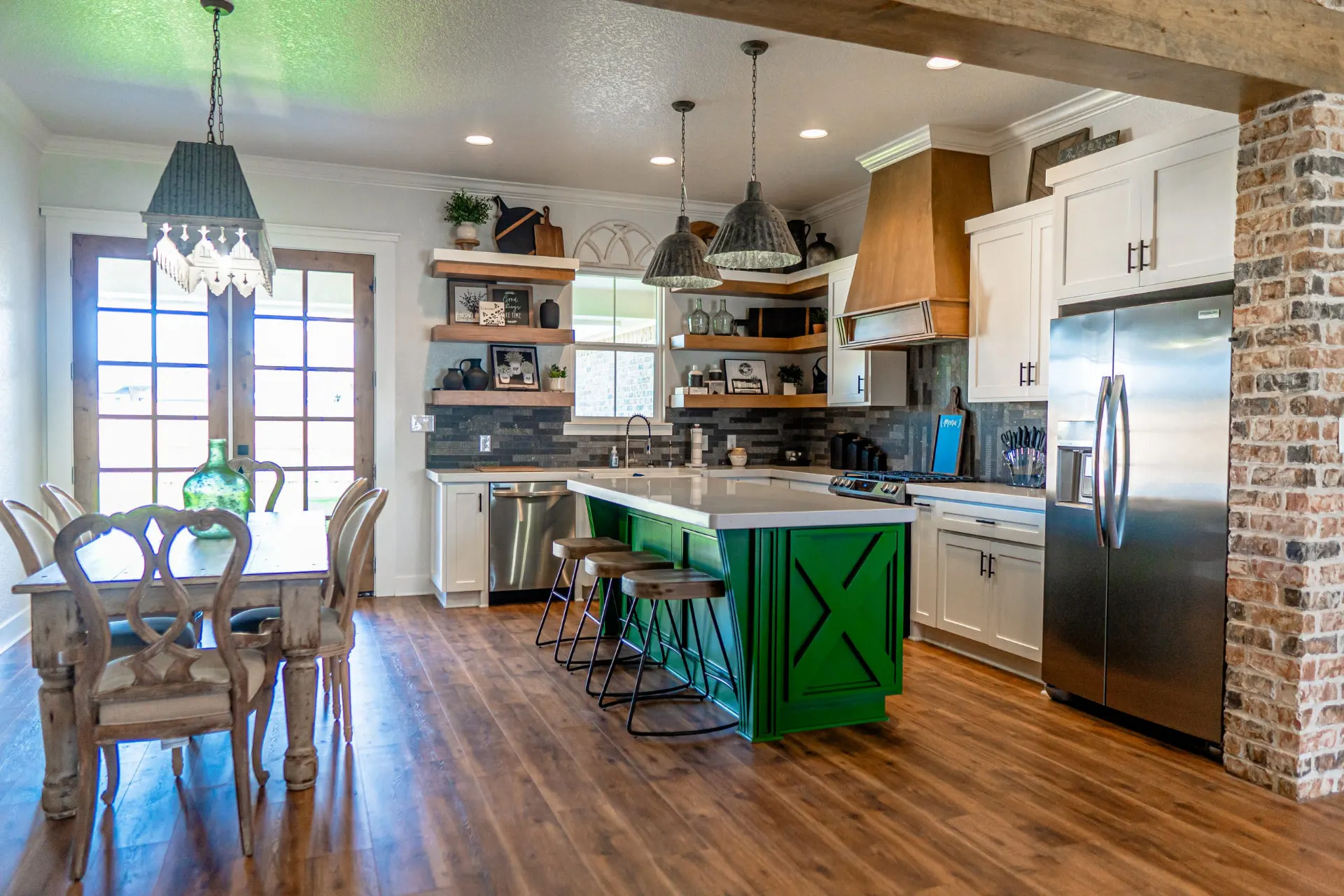 Kitchen at the K Ave Farmhouse with a green barn-door island, white cabinetry, a copper-toned wood hood and an adjoining dining table under a black pendant