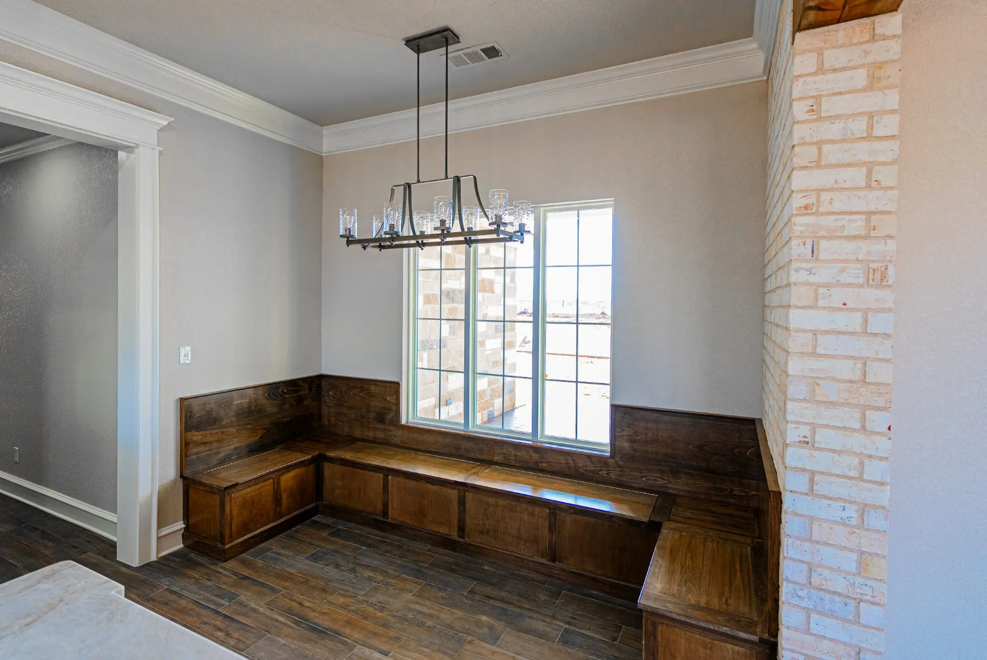 Breakfast nook at 1602 NW 12th St with stained-wood built-in banquette, linear chandelier and whitewashed brick accent