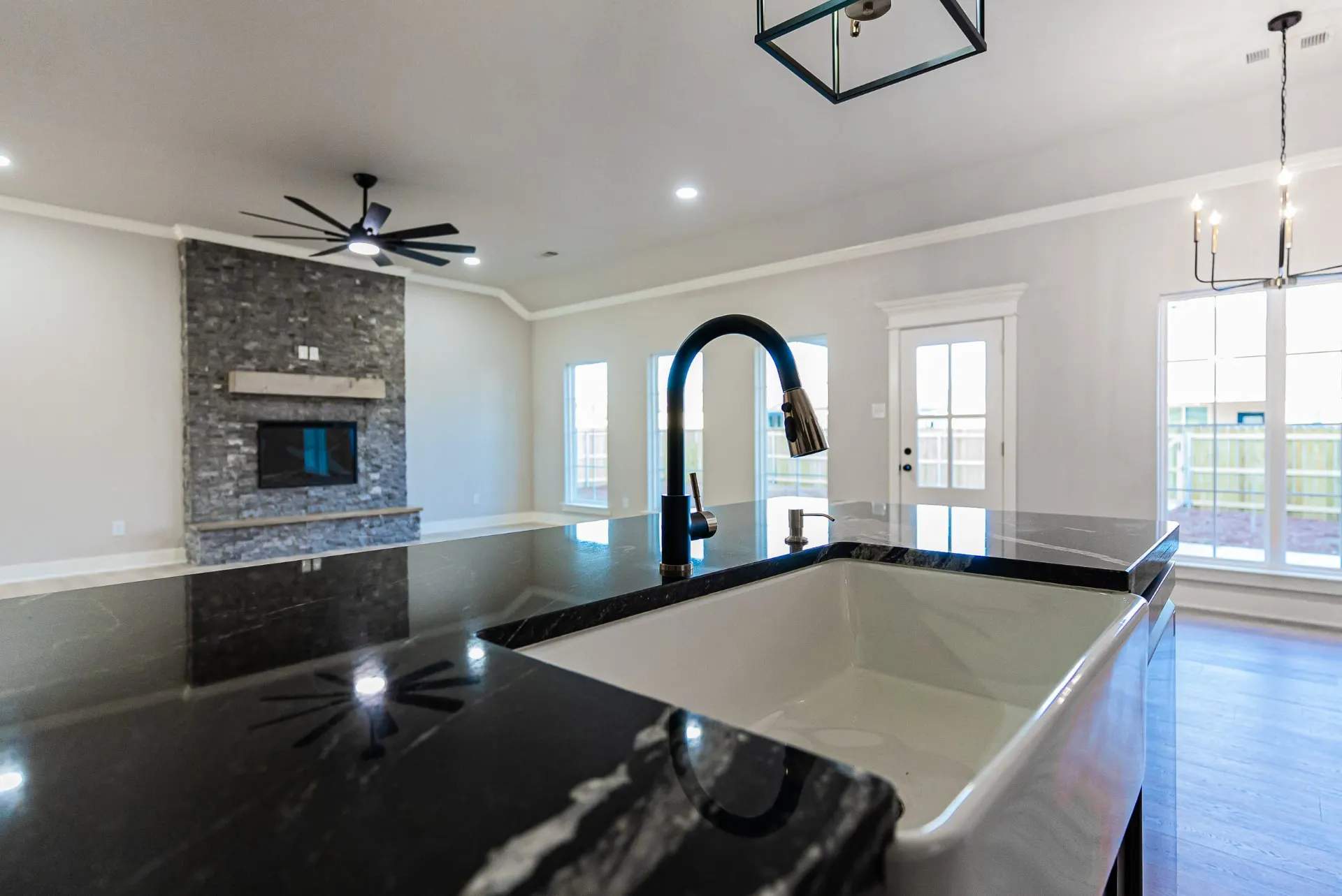 Black marble island at 708 K Ave with a white farmhouse sink, matte black faucet and a view across the great room to the stone fireplace