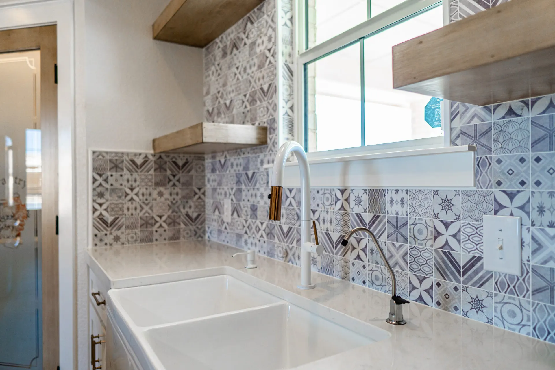 Close-up of the Sarai Home kitchen sink with a white gooseneck faucet with brass tip against hand-painted patterned tile