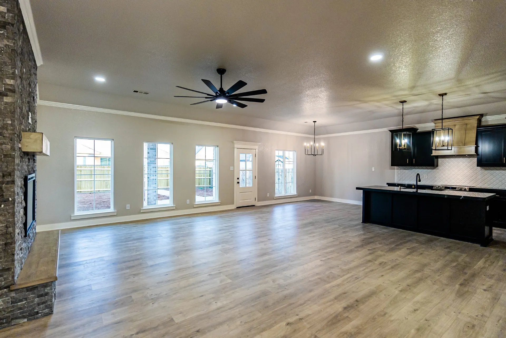 Open great room and kitchen at 708 K Ave with black cabinetry, stacked-stone fireplace wall and wood-look floors