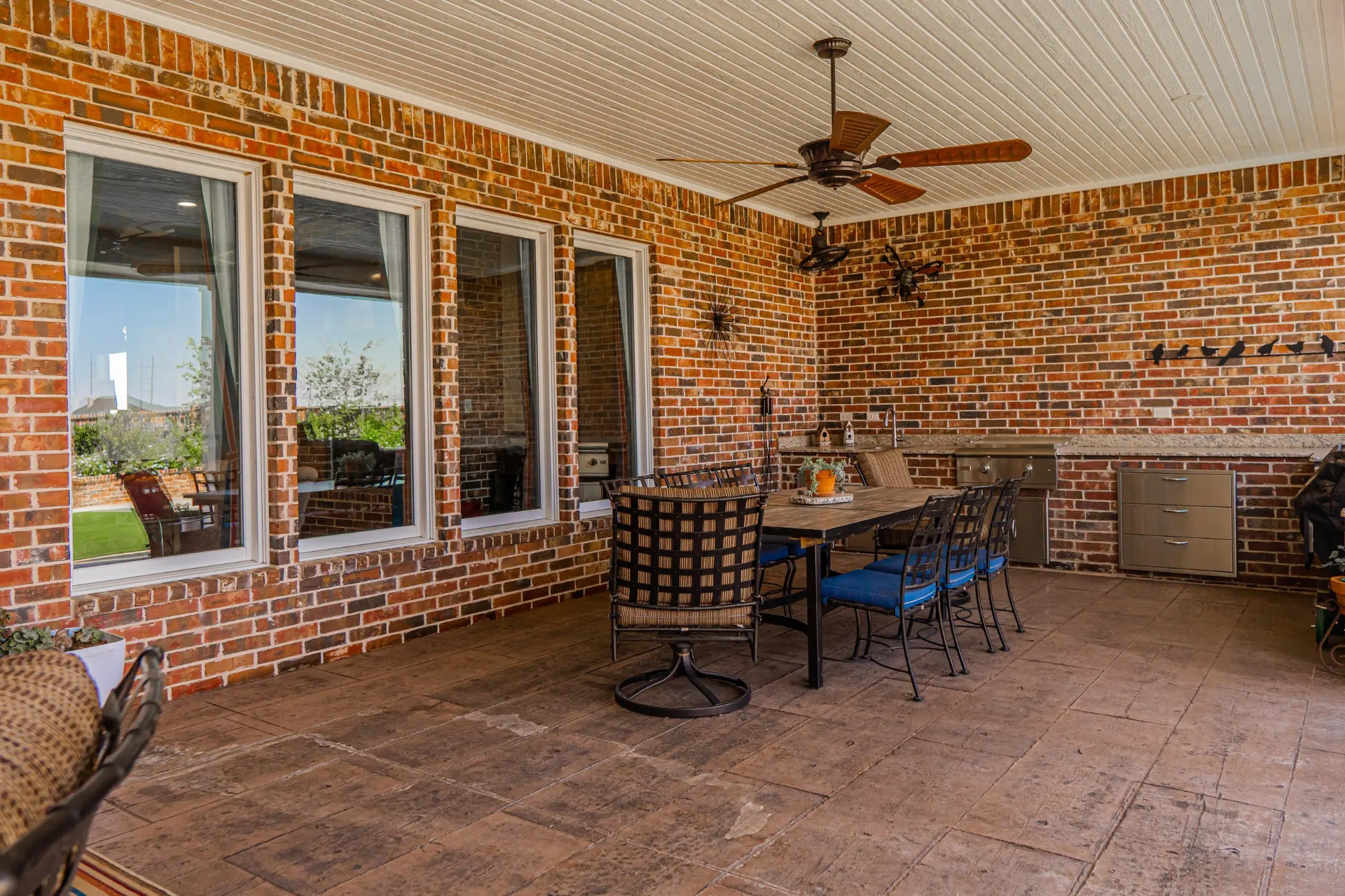 Covered back patio at the Wraparound Porch Home with a beadboard ceiling, outdoor dining table and a built-in grill station with stainless drawers