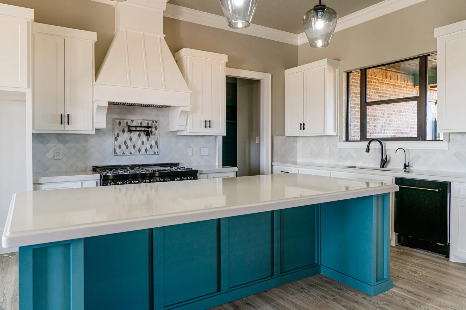 Kitchen at the 12th St Home with a deep teal island and oversized white quartz top, white shaker cabinets, a white hood over a black range and a herringbone tile backsplash with a diamond mosaic inset