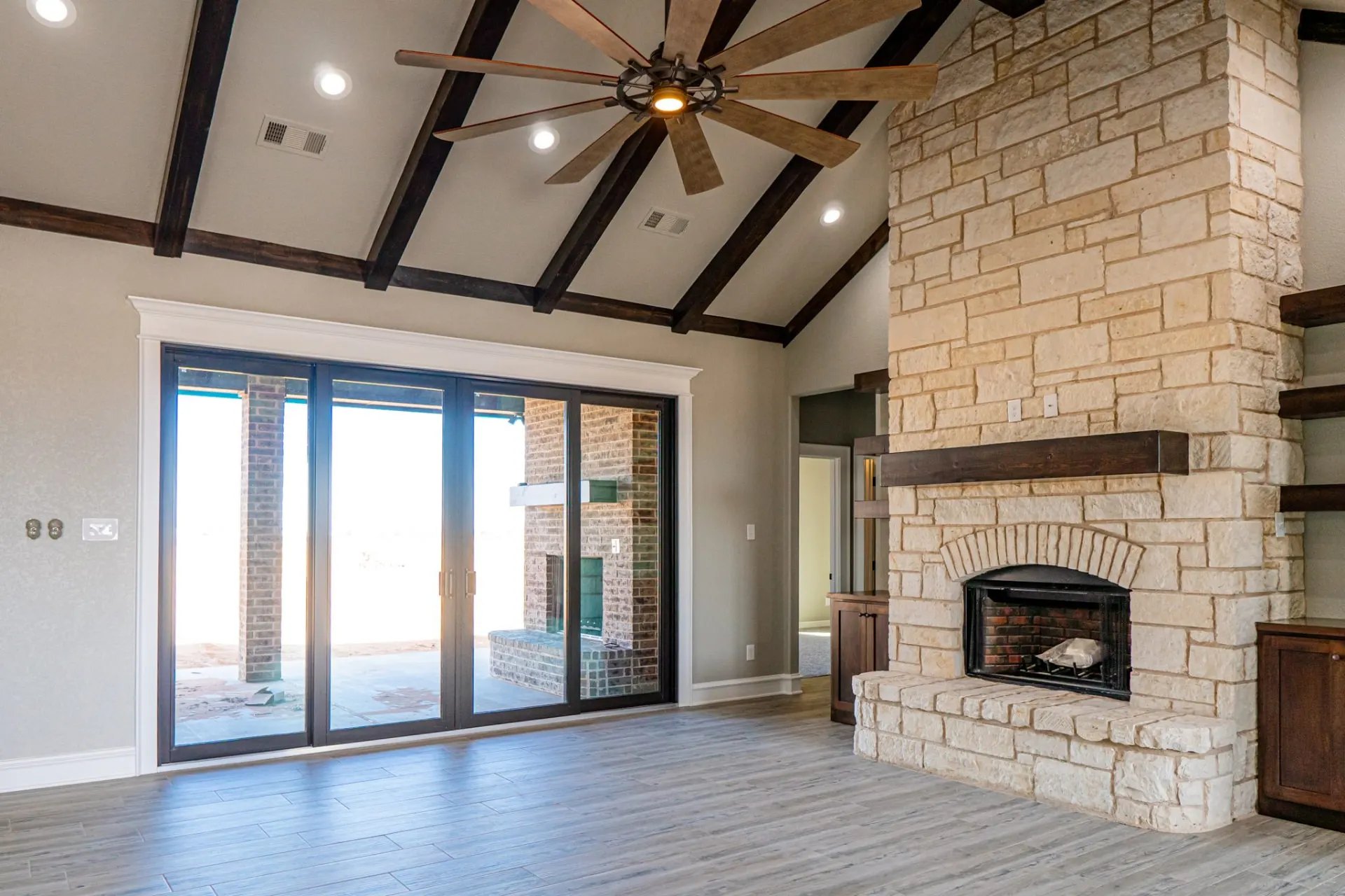 Great room at the 12th St Home from above, showing the dark beamed vaulted ceiling, eight-blade fan and stone fireplace with dark built-ins