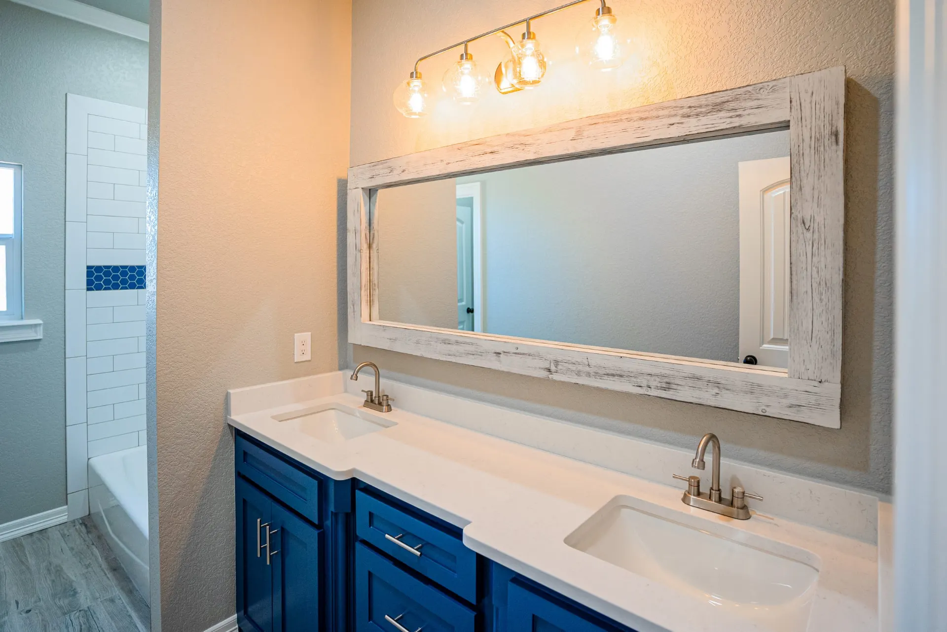 Secondary bath at the Eliam St Home with a cobalt blue double vanity, white quartz counters and a whitewashed wood-frame mirror