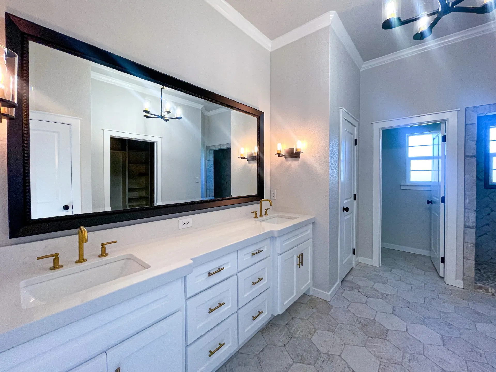 Primary bath at 1615 NW 12th St with double vanity, brass fixtures, black-framed mirrors, hexagon tile floor and glass-enclosed shower