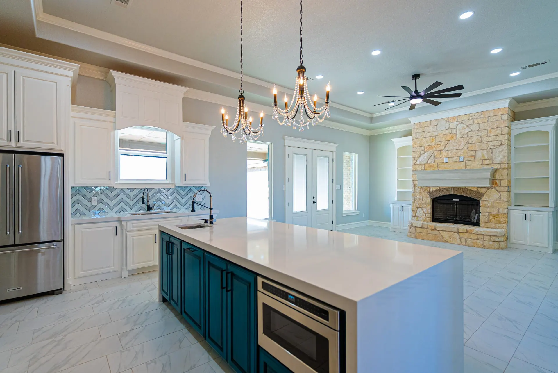 Wide kitchen at 1511 NW 12th St with twin chandeliers over the teal island and a stone fireplace beyond