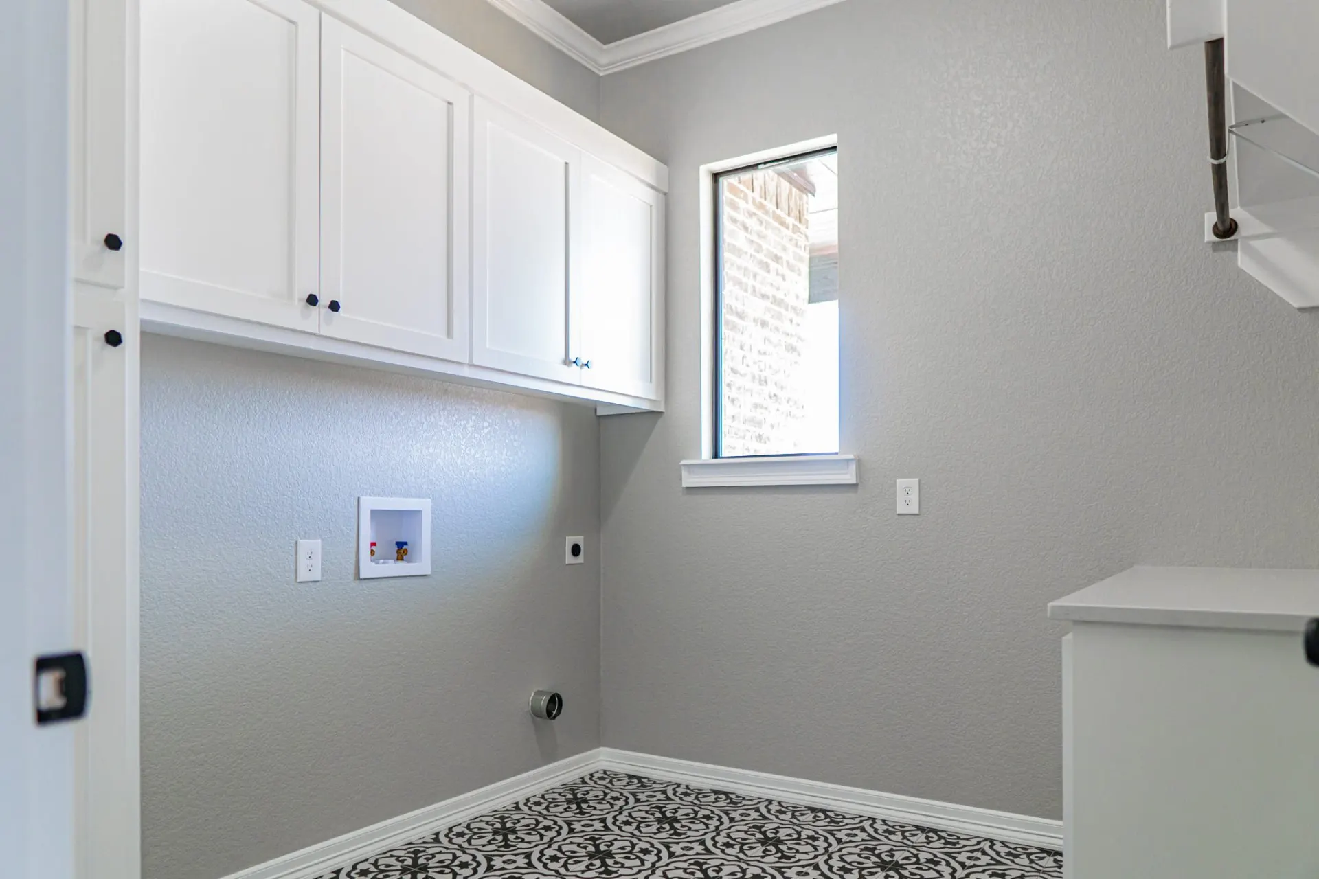 Laundry room at the 12th St Home with white upper cabinets, a folding counter and black-and-white patterned tile floor