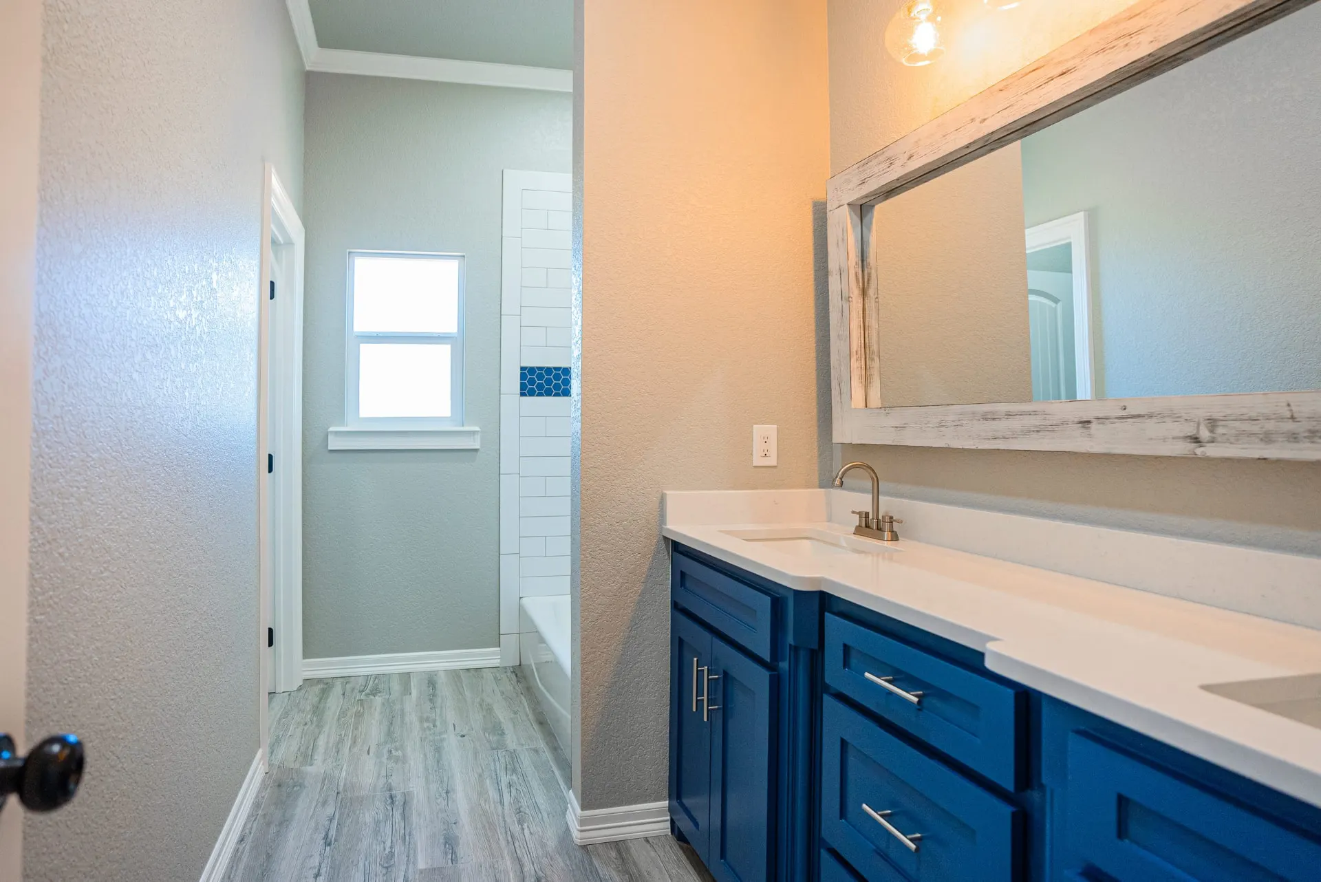 Bathroom at the Eliam St Home seen from the door, with the cobalt vanity and whitewashed mirror on the right and the tub shower and window down the hall