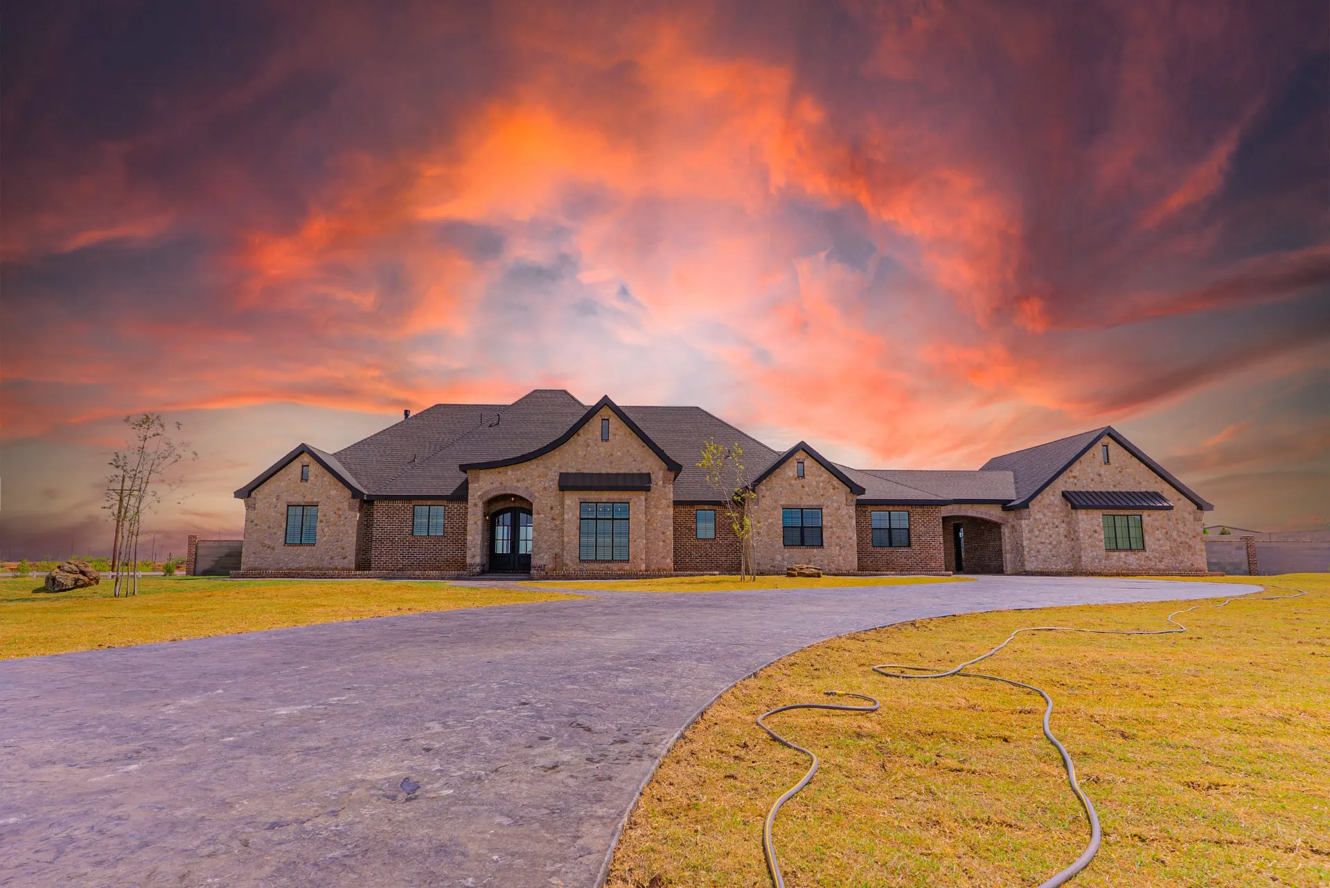 Front elevation of 1610 NW Eliam Dr at sunset, with stone and brick gables and a curved stamped-concrete drive