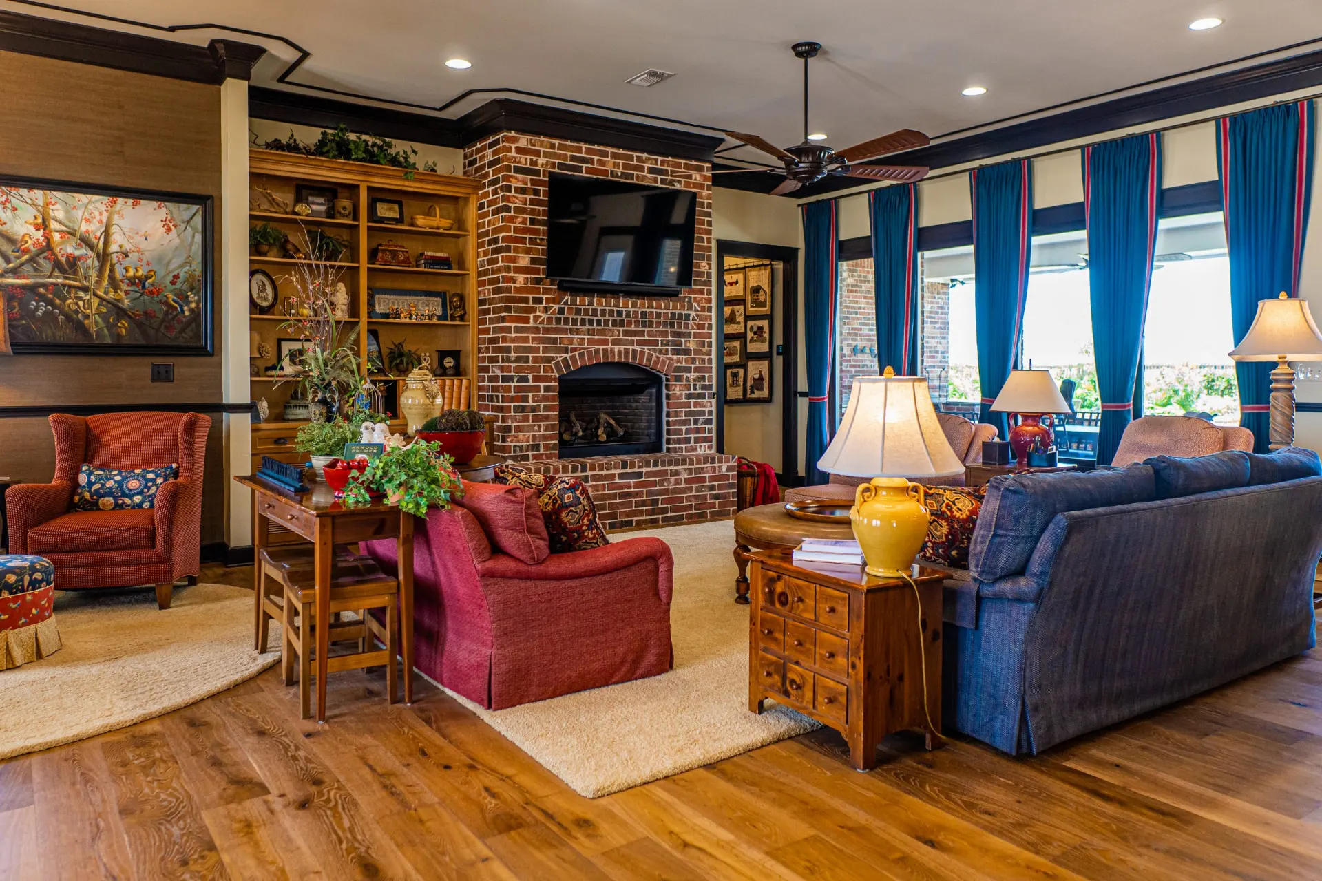 Family room at the Wraparound Porch Home with an arched brick fireplace, built-in oak shelving, layered seating and teal drapery with red trim
