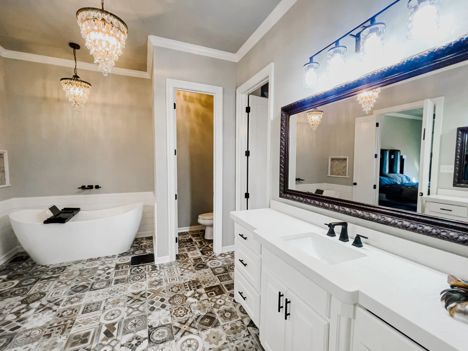 Primary bath at 8821 Shawn Dr with a white freestanding tub and wall-mounted black fixtures against white shiplap, twin crystal chandeliers, a white double vanity and intricate patterned floor tile