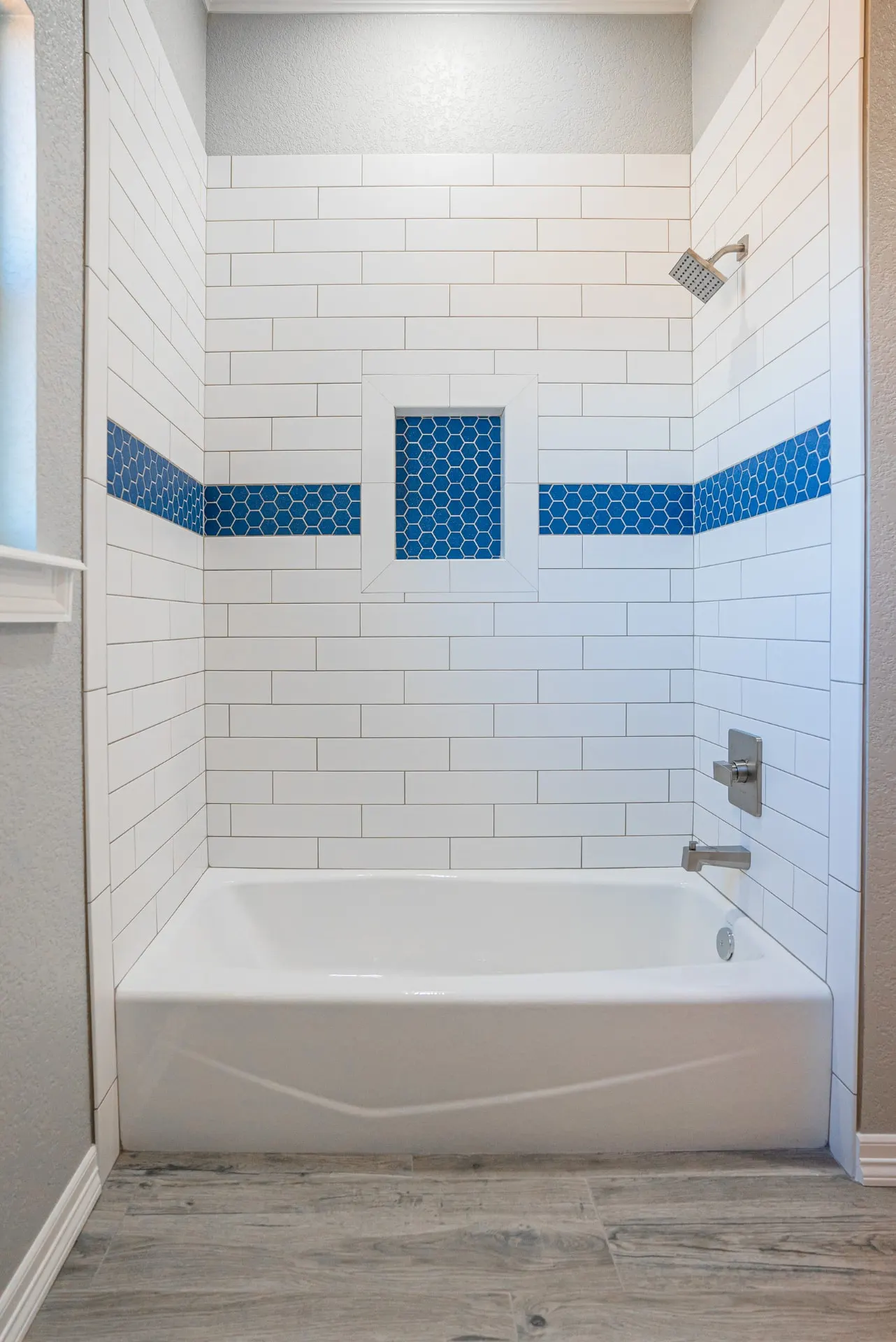 Straight-on view of the Eliam St Home tub with white subway walls, twin cobalt hexagon accent bands, a framed blue mosaic niche and brushed-nickel fixtures