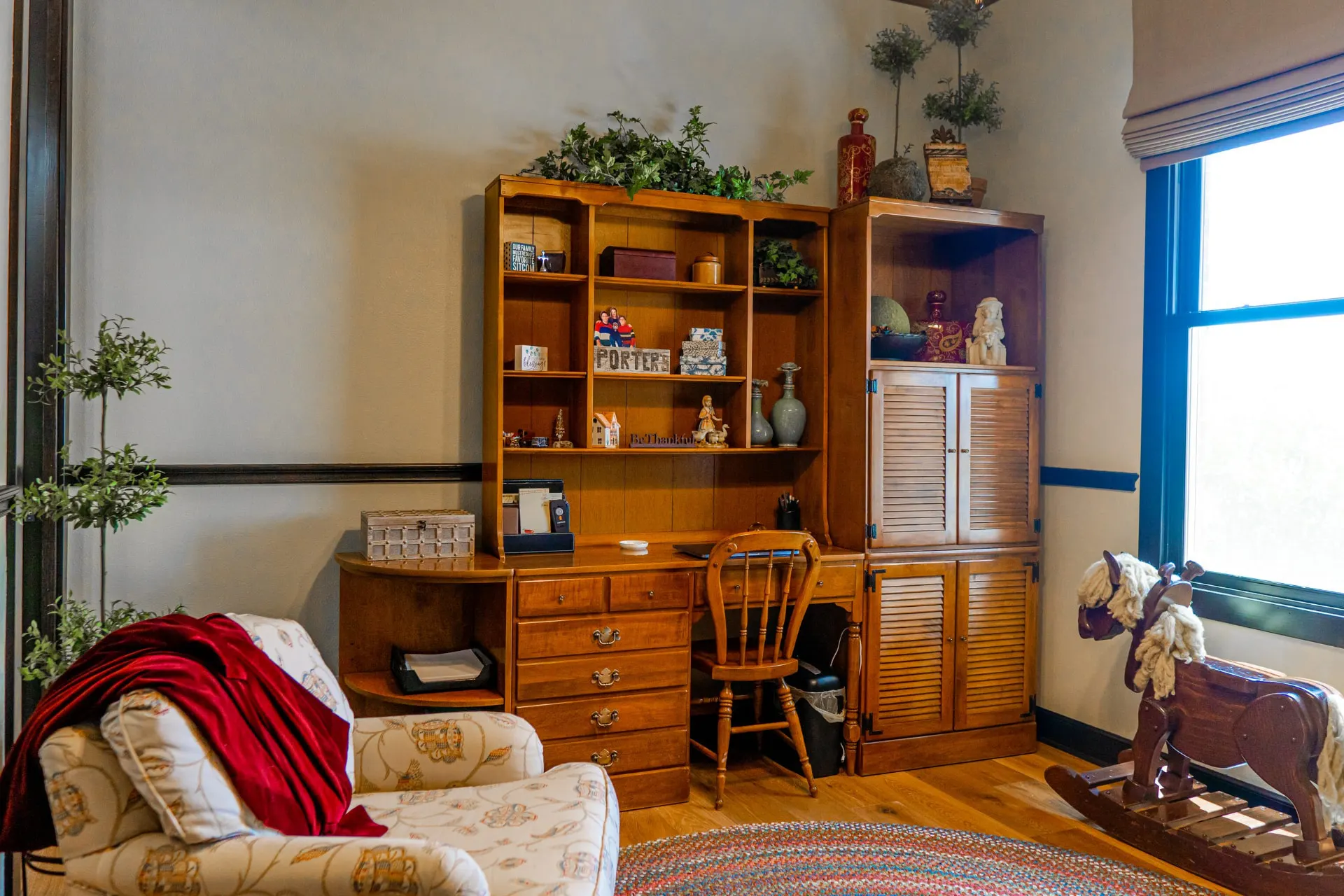 Honey-oak desk nook with a hutch, louvered cabinet and spindle chair in the mural bedroom at the Wraparound Porch Home, with a wooden rocking horse by the window