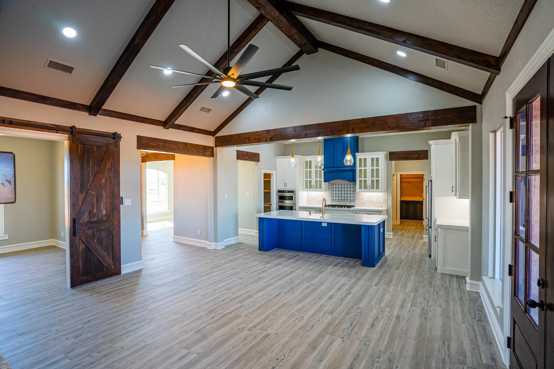 Great room at the Eliam St Home with dark wood trusses over the kitchen's cobalt blue island and hood, white perimeter cabinetry and barn doors