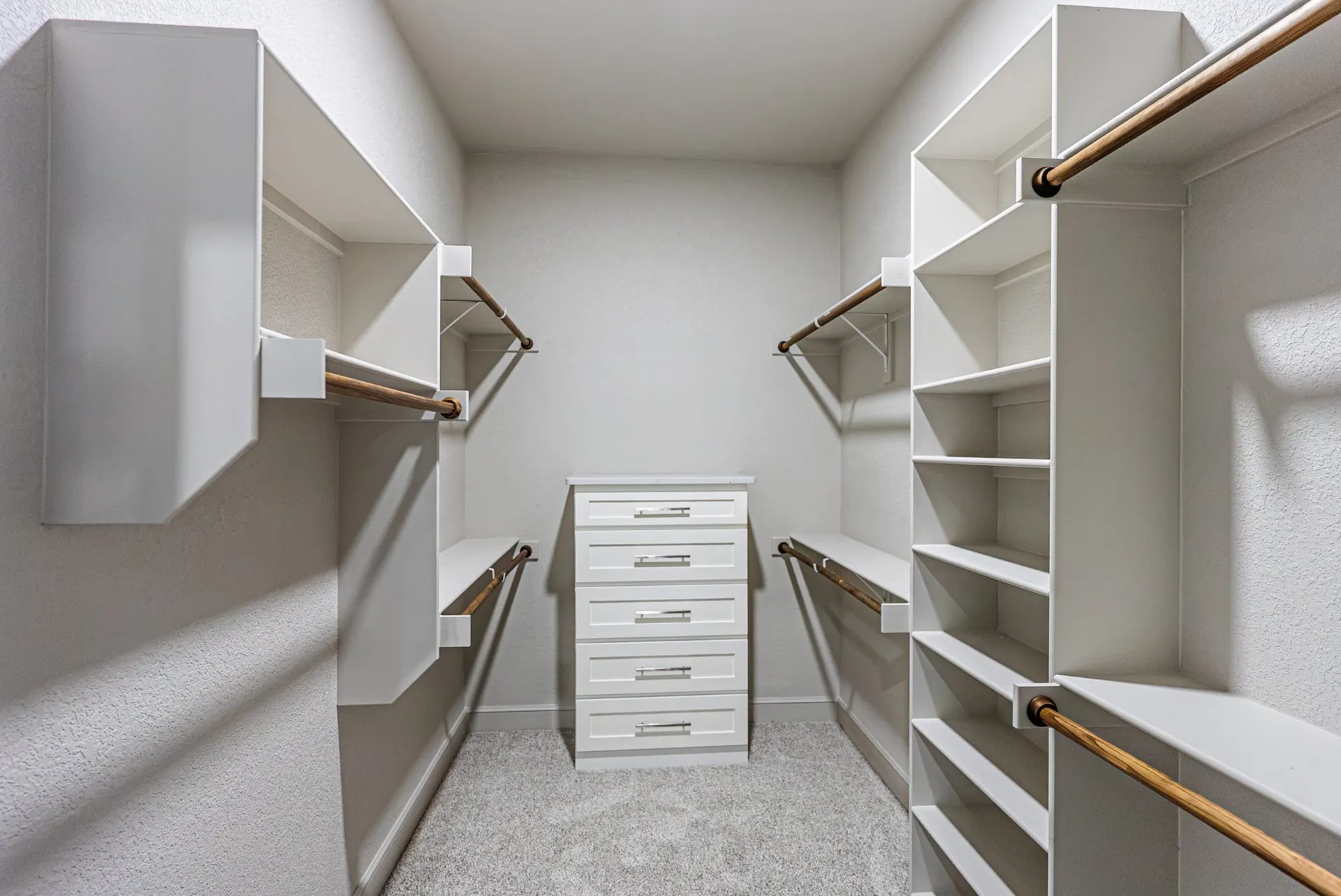Primary walk-in closet at 27 Santiago Mission Dr with a white organization system, layered hanging rods and a central drawer tower