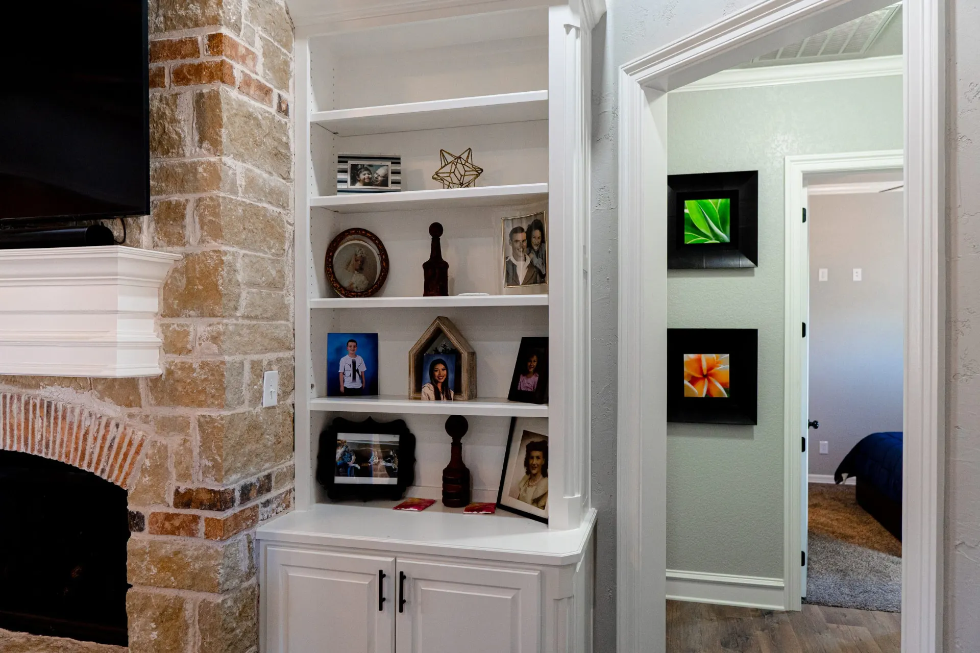 Living room at 8821 Shawn Dr with white built-in shelving beside a stone and brick fireplace hearth, opening to a hallway with framed wall art