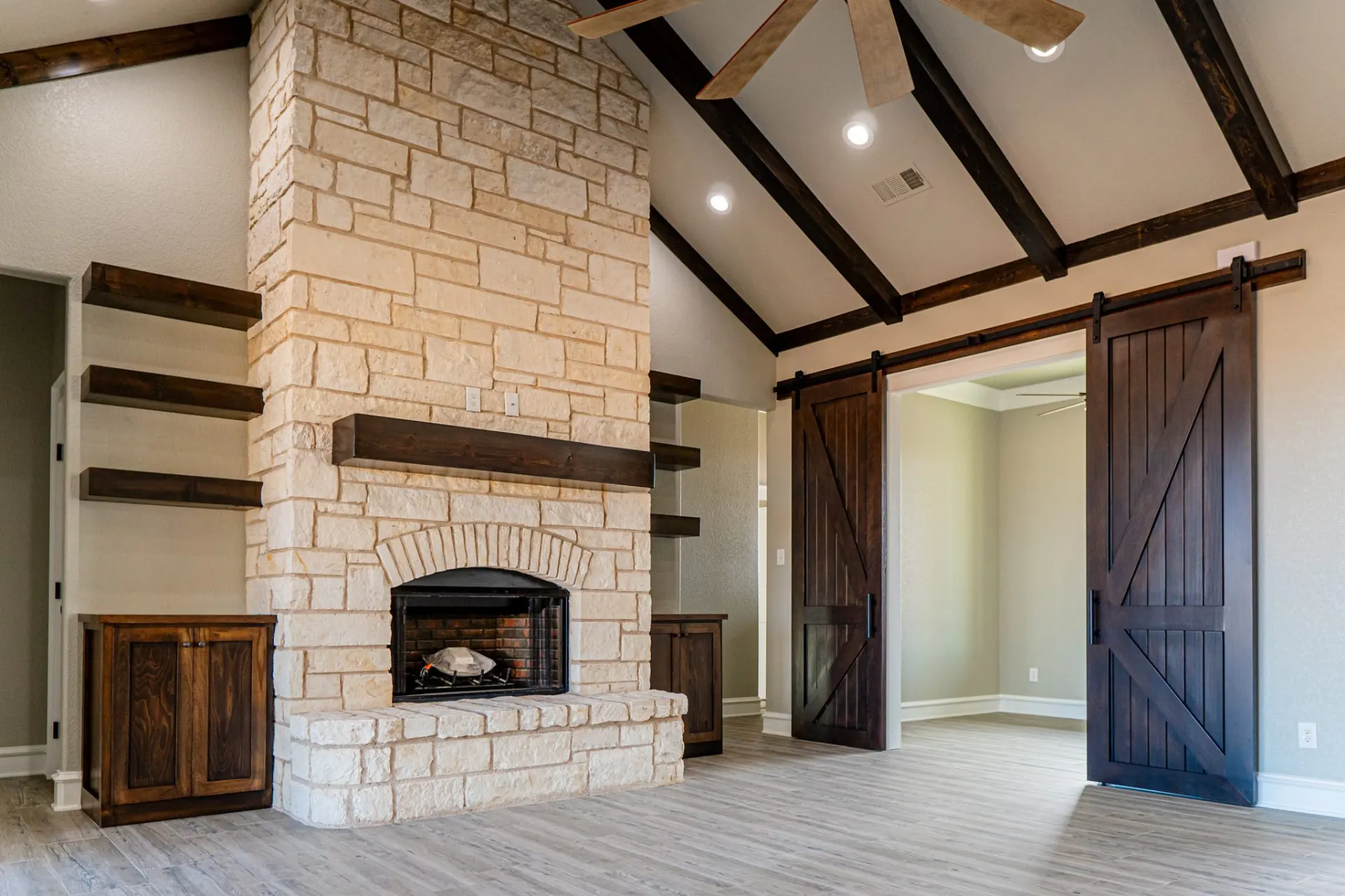 Fireplace wall at the 12th St Home with dark floating shelves and double stained barn doors opening to the room beyond