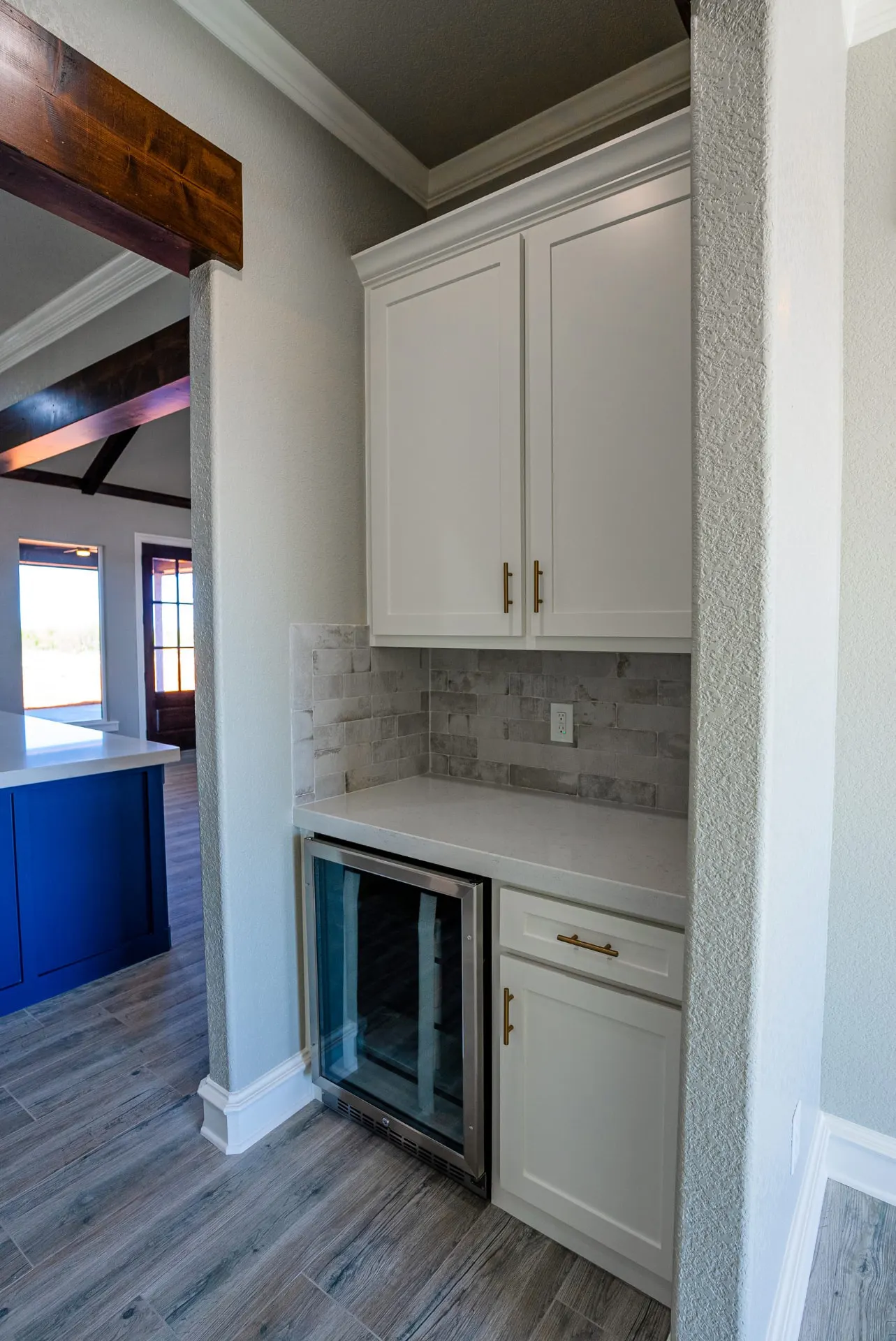 Coffee bar at the Eliam St Home with white cabinetry, brass pulls, a grey subway-tile backsplash and a glass-door beverage fridge
