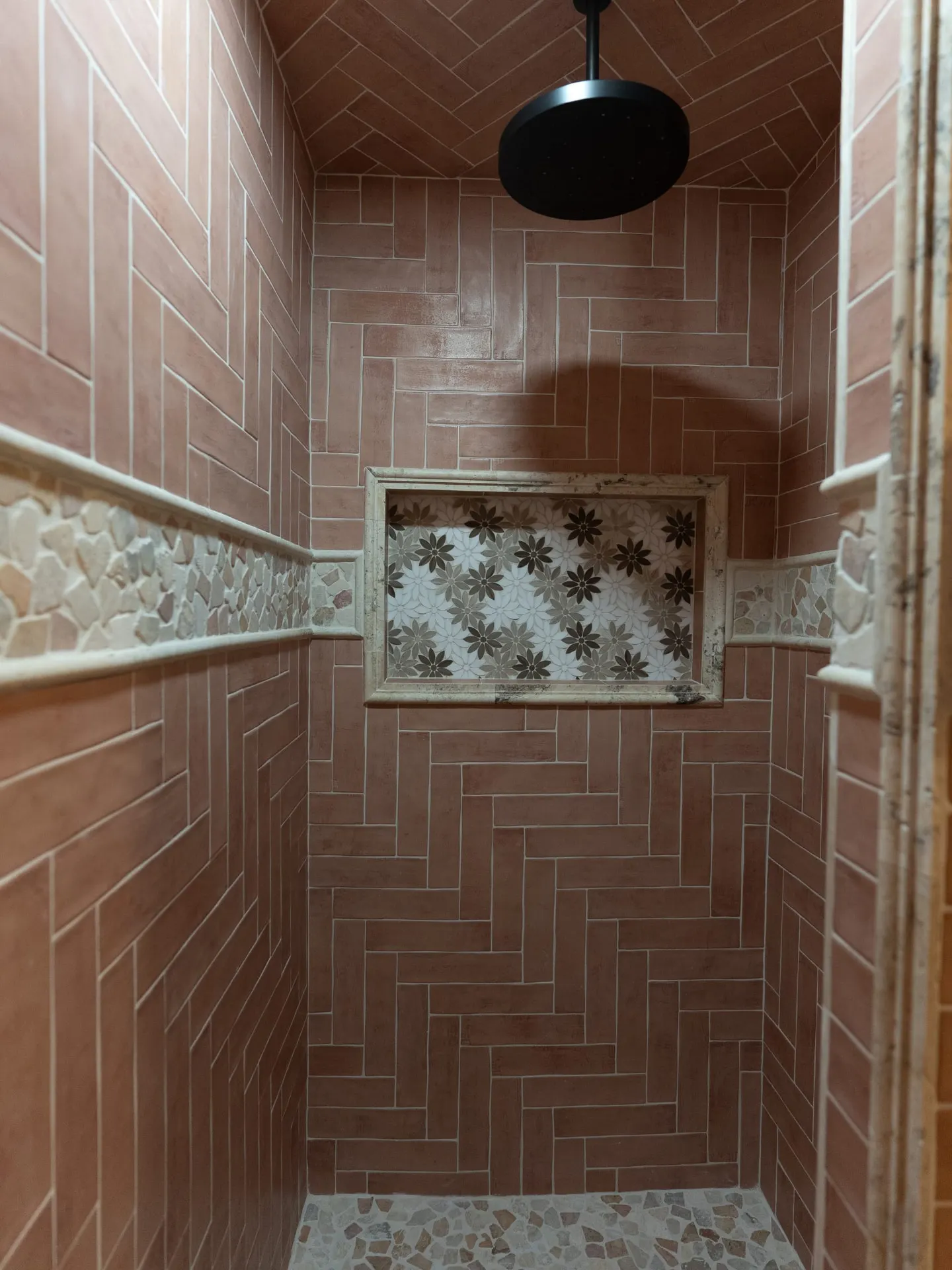Walk-in shower at 1610 NW Eliam Dr with terracotta herringbone tile, pebble floor and floral mosaic niche