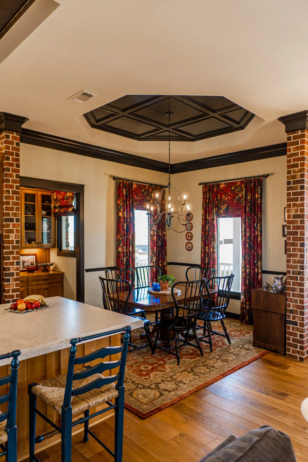 Dining room at the Wraparound Porch Home framed by brick columns, with an octagonal coffered ceiling and a lit glass-front hutch